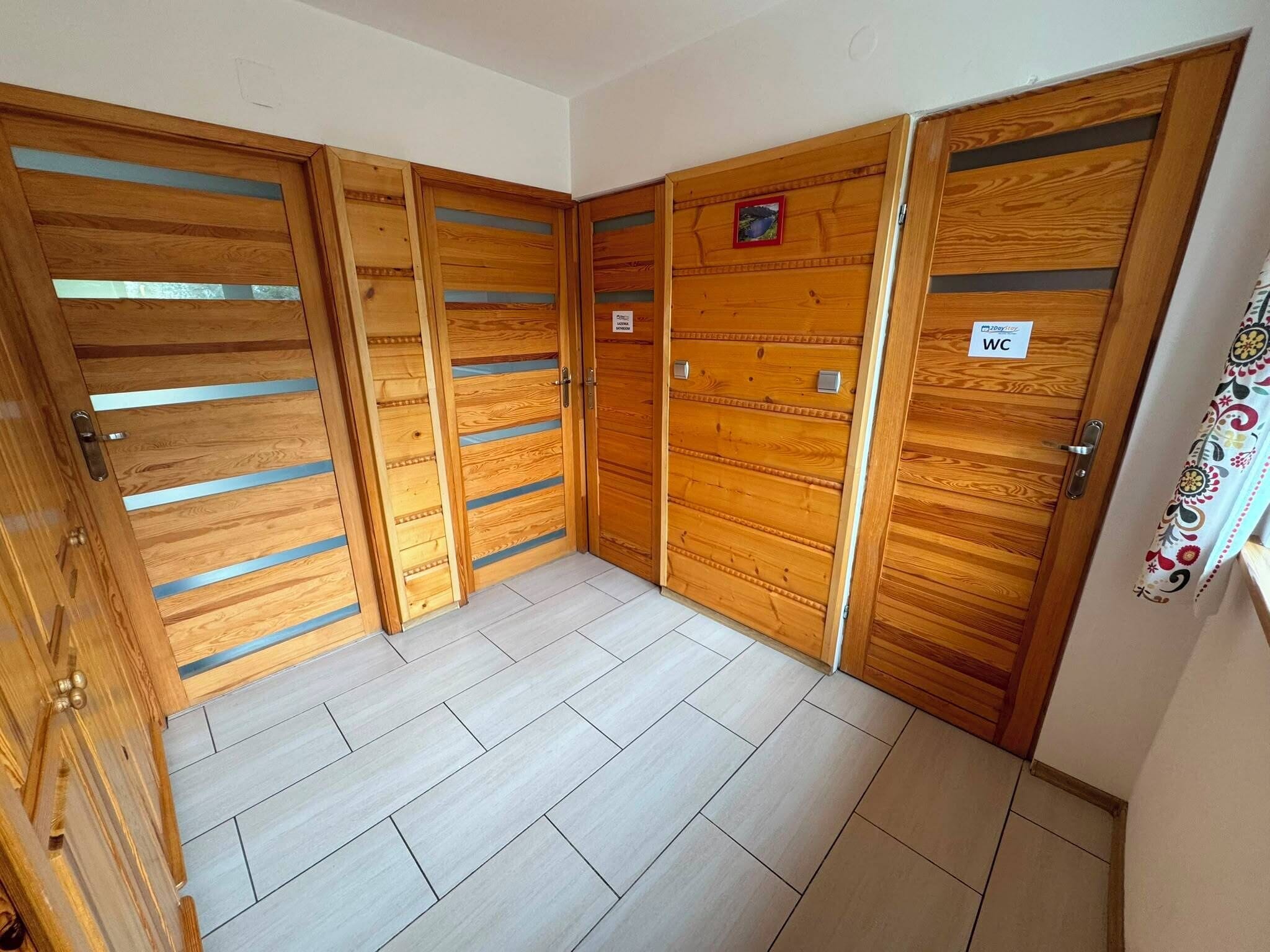 Un conjunto de puertas de madera con un cartel que indica un aseo, un suelo de baldosas y una pequeña foto en la pared.