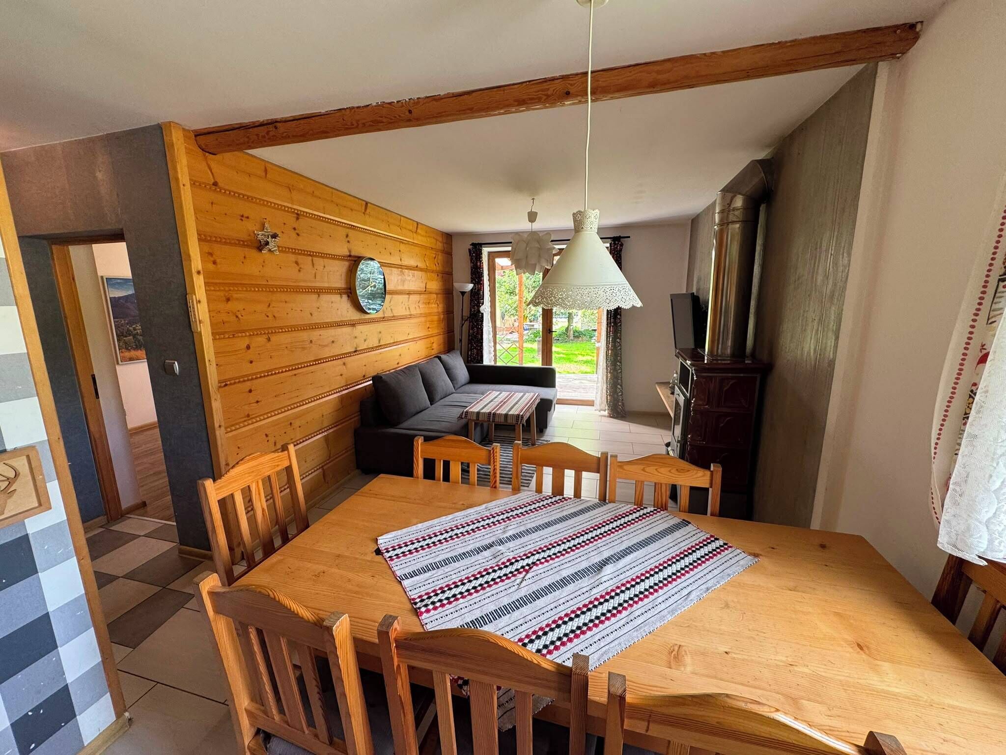 A dining area with a wooden table, chairs, a sofa, and a hanging light fixture.