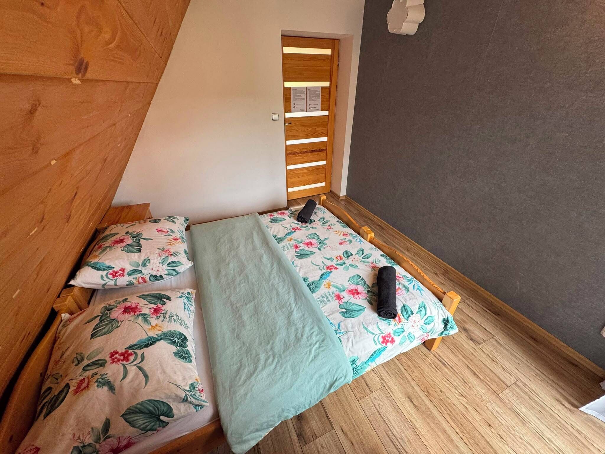 Una habitación pequeña y acogedora con techo inclinado, un armario de madera, una cama con ropa de cama floral y una ventana con persianas.