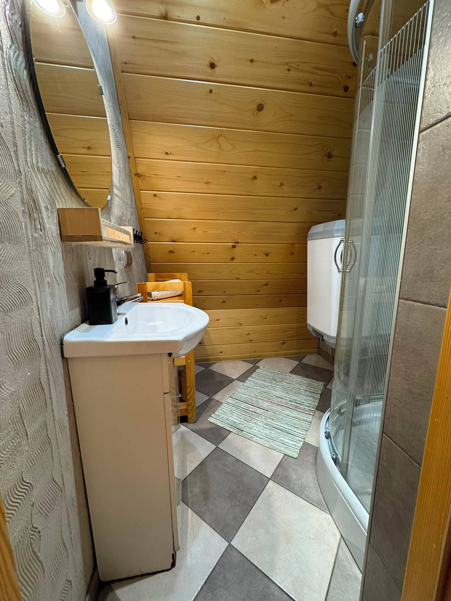 A compact bathroom with a wooden interior, a white sink, a toilet, and a shower enclosure.