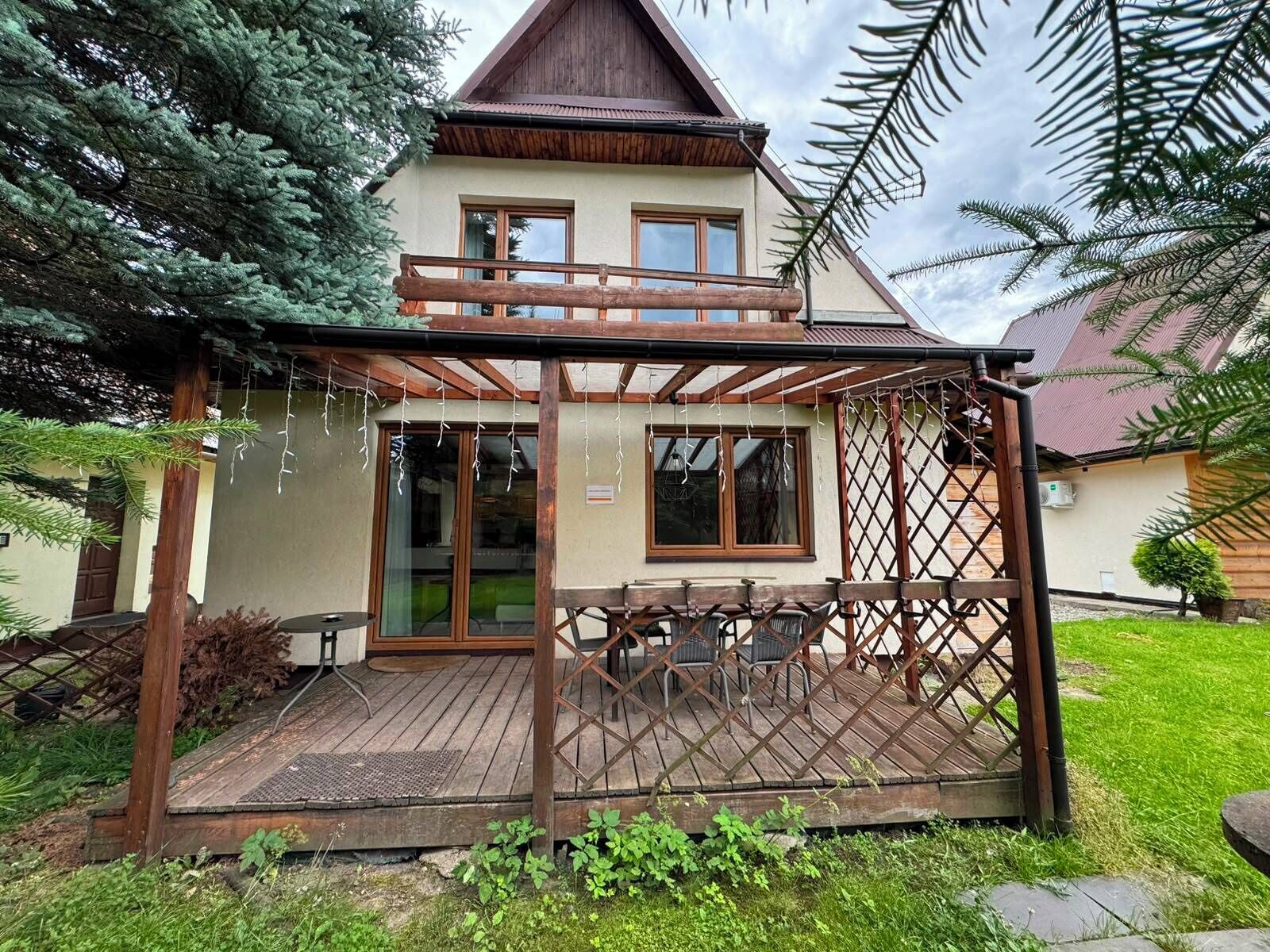 A wooden deck with a covered seating area, a house with a sloped roof, and a well-maintained garden.
