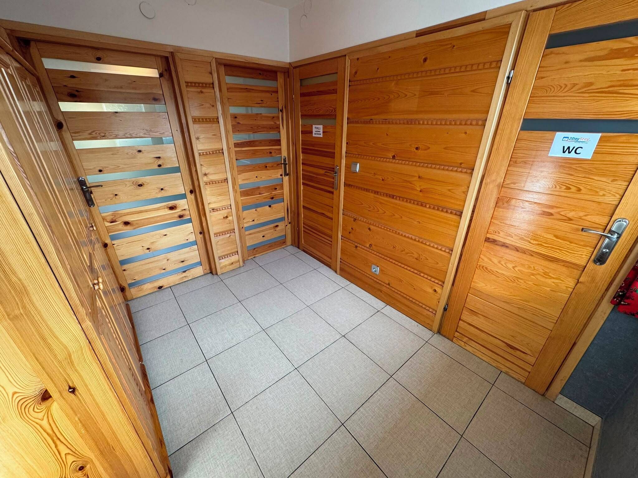Un pasillo con puertas de madera, suelo de baldosas y un letrero que indica un baño.