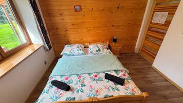 Un lit en bois avec une literie à motifs floraux, dans une pièce dont le plafond est également en bois et qui possède une fenêtre avec des rideaux.