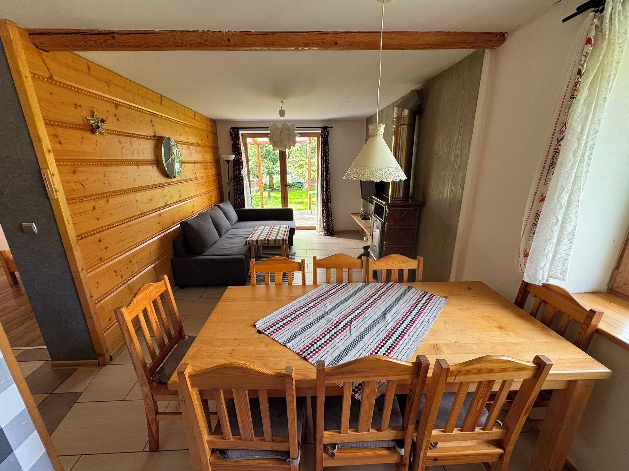 A dining area with a wooden table, chairs, a sofa, and a patterned table runner.