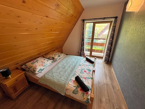 A bedroom with a wooden sloped ceiling, a bed with floral bedding, a nightstand, and a window with curtains. - 2DayStay - ZKP (Zakopane)
