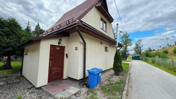 A single-story building with a brown door and a number '12' on the wall, a blue trash bin, and a gravel driveway.