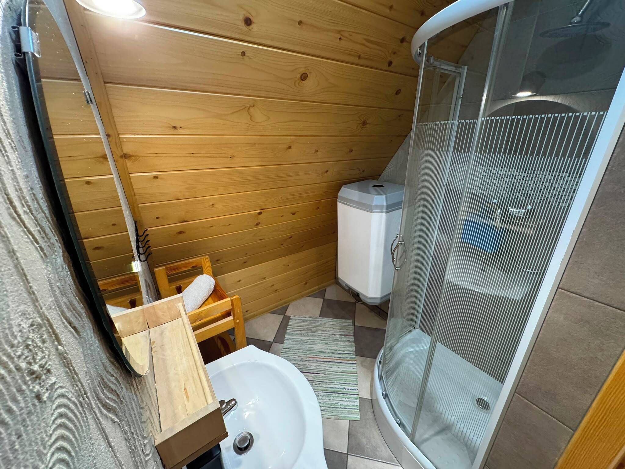 Un baño pequeño con paredes de madera, cabina de ducha y lavamanos.
