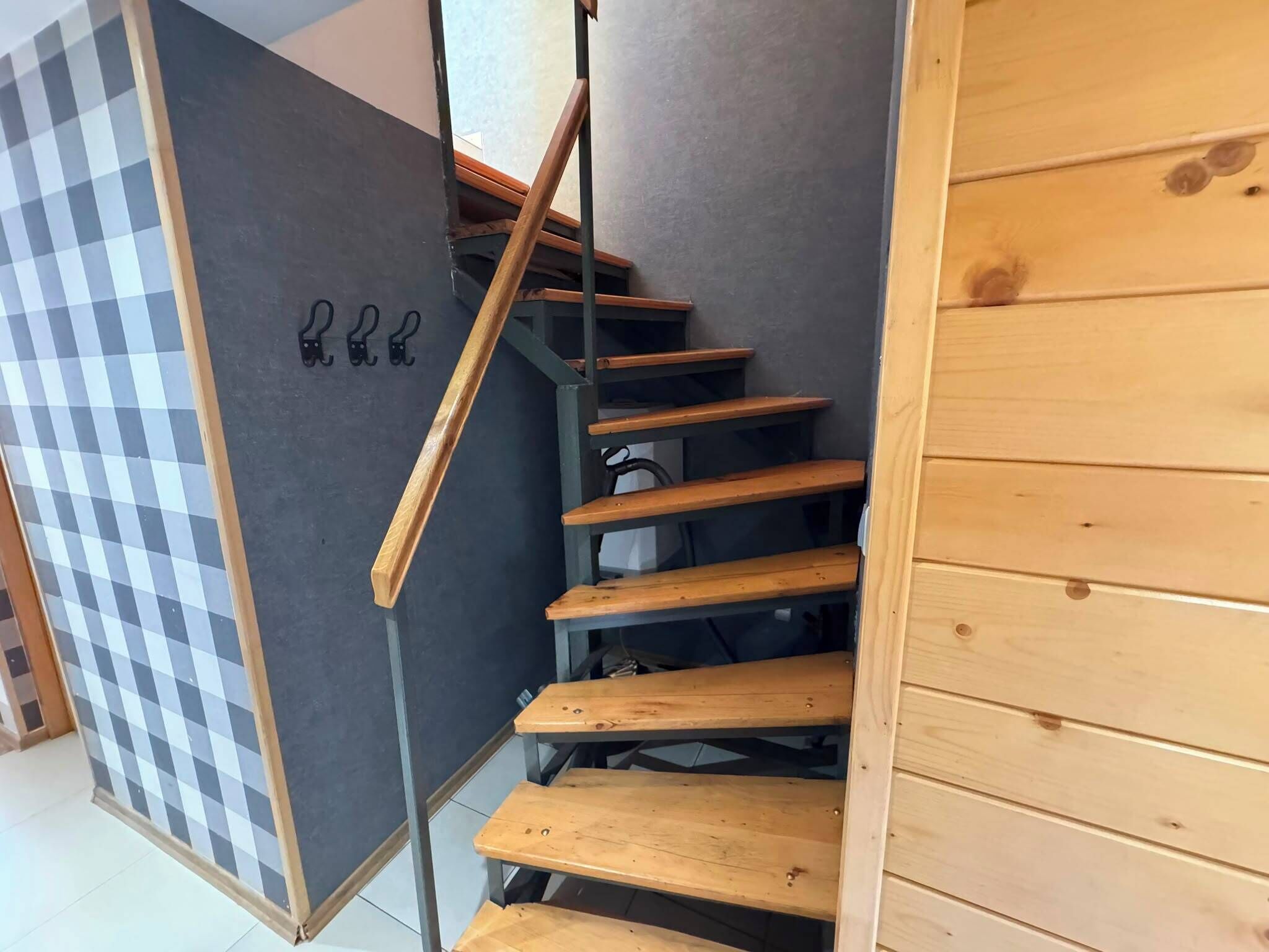 A wooden staircase with a checkered floor pattern on the left and a plain wall on the right.