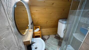 A bathroom with a wooden wall, a sink, a mirror, a shower enclosure, and a toilet.