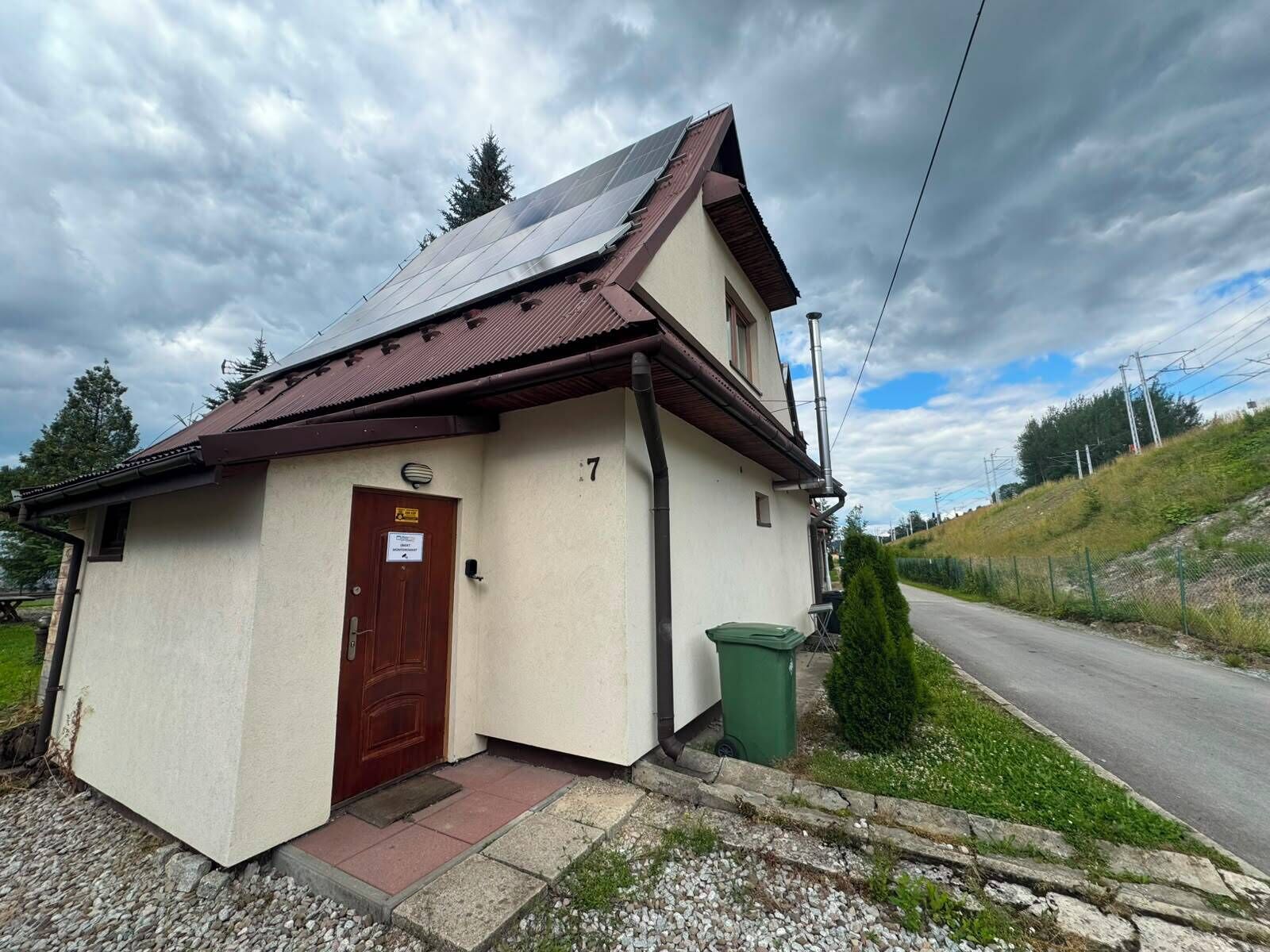 A small building with a brown door, a number '7' on the wall, and a green trash bin.