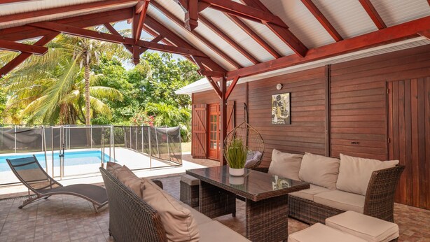 A covered outdoor seating area with a pool, wicker furniture, and a wooden wall. - L'Echappée Tropicale - Maison avec piscine privée (Le Moule)