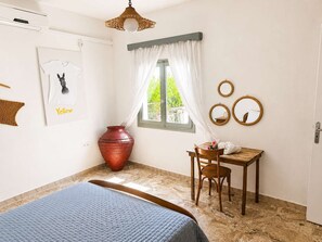 A room with a bed, a desk with a chair, a window with curtains, a wall-mounted mirror, and a large vase. - The Yellow Donkey, Koumeika Traditional Gem Samos (Koumeika)