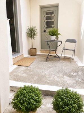 A small outdoor seating area with a table and chairs, a door, and two potted plants. - The Yellow Donkey, Koumeika Traditional Gem Samos (Koumeika)
