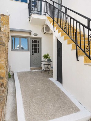 A narrow courtyard with a staircase leading to an upper floor, a door with a decorative pattern, and a small table with a plant. - The Yellow Donkey, Koumeika Traditional Gem Samos (Koumeika)