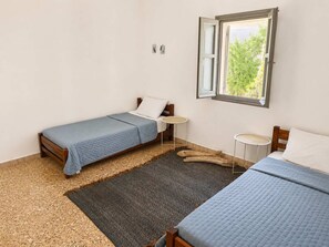 Ein Schlafzimmer mit zwei Betten, einem kleinen Tisch, einem Spiegel und einem Fenster mit Blick auf Grünflächen.