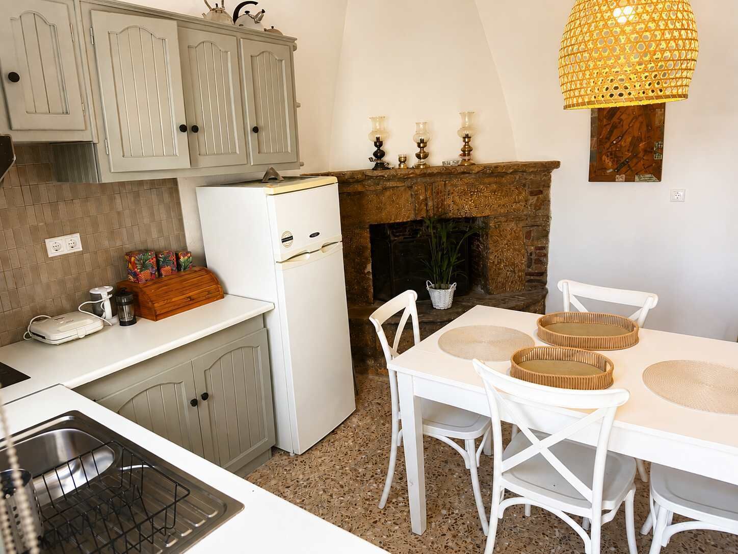 A kitchen with a white refrigerator, a dining table with white chairs, and a hanging light fixture.