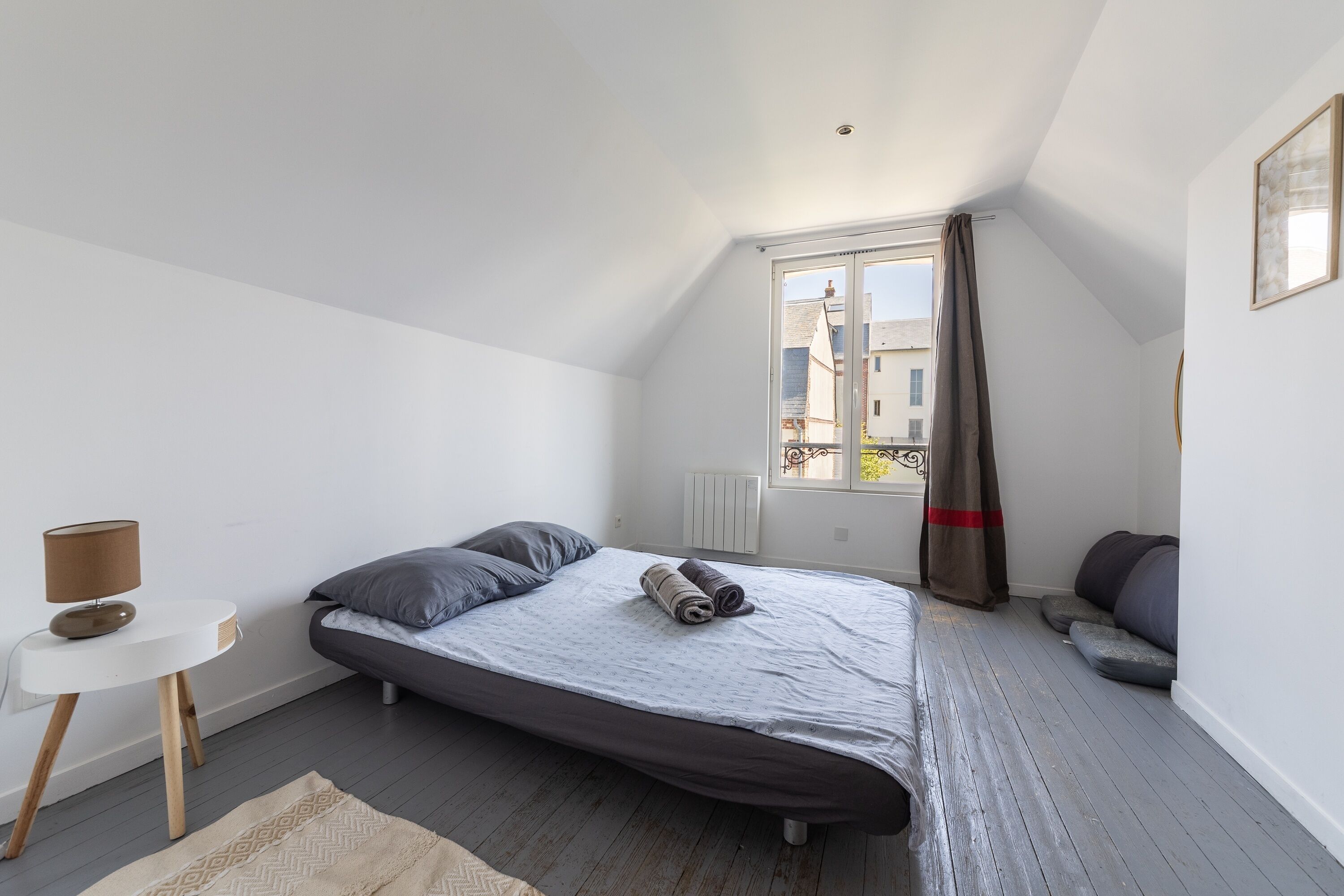 Un dormitorio con cama, una mesita de noche con lámpara, una ventana con cortinas y vistas a edificios.