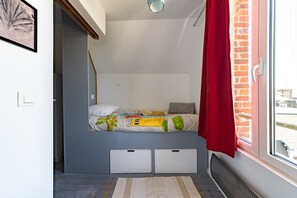 Ein kleines Zimmer mit einem Etagenbett, einem Fenster mit rotem Vorhang und Blick ins Freie.