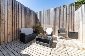 Een terras met een zwarte bank, een rieten stoel en een klein tafeltje met een decoratief object.