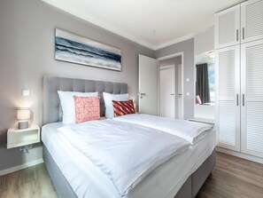 A modern bedroom with a large bed, a bedside table with a lamp, a wardrobe with sliding doors, and a painting on the wall. - Geraumige Wohnung mit Uberdachter Terrasse (Lübeck)