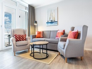 A modern living room with a grey sofa, two armchairs, a coffee table, and a painting of sailboats. - Geraumige Wohnung mit Uberdachter Terrasse (Lübeck)
