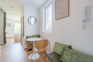 Ein modernes Wohnzimmer mit rundem Tisch, einer Couch, einem Sessel und einem großen Fenster.