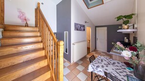Eine Holztreppe führt zu einem Raum mit einem Heizkörper, einem Tisch mit einer blumigen Tischdecke und einer Topfpflanze.