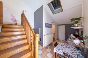 A wooden staircase leading to a room with a radiator, a table with a floral tablecloth, and a potted plant. - Le Gîte Mezzanine - À 30 min du Futuroscope (Chalandray)