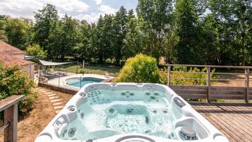A hot tub with a wooden deck and a pool in a backyard with trees.