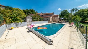 Ein rechteckiger Pool mit gefliestem Rand, umgeben von einem Zaun und Bäumen.