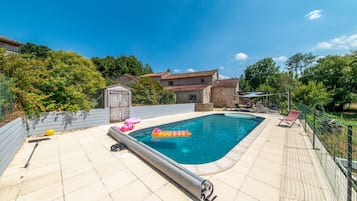 A rectangular swimming pool with a tiled deck, surrounded by a fence and trees.