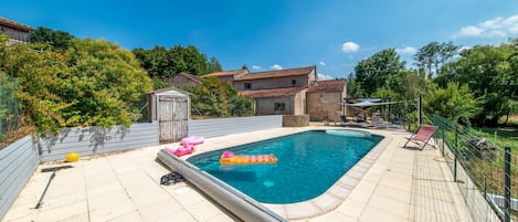 Ein rechteckiger Pool mit gefliestem Rand, umgeben von einem Zaun und Bäumen.