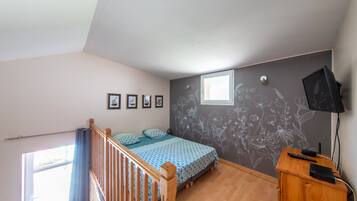 A bedroom with a bed, a wooden desk, a TV, and a window.