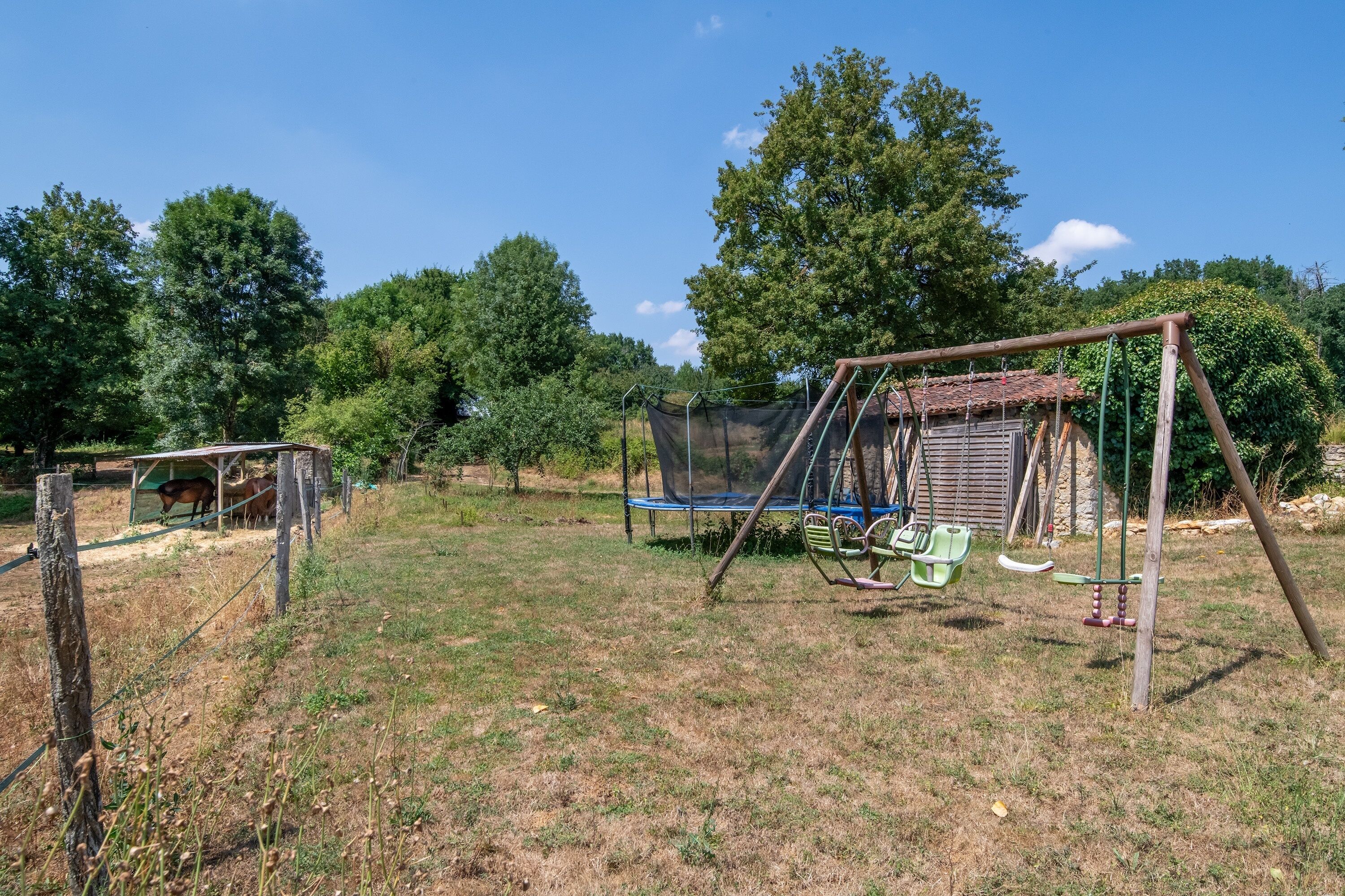 A fenced outdoor area with a swing set, a trampoline, and a horse enclosure.