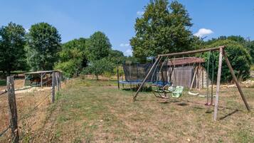A fenced outdoor area with a swing set, a trampoline, and a horse enclosure.