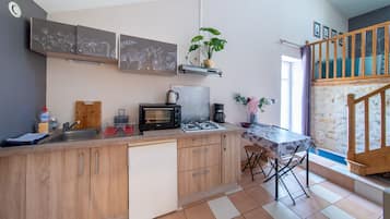 A compact kitchen with a built-in dishwasher, a gas stove, a coffee maker, and a small dining area with a table and chairs.