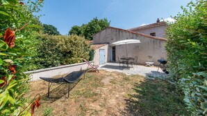 Ein rustikales Haus mit Terrasse, Grill und Liegestuhl.