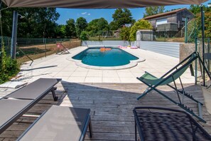 A swimming pool with a wooden deck, lounge chairs, and a covered area. - Le Gîte Maisonnette - À 30 min du Futuroscope (Chalandray)