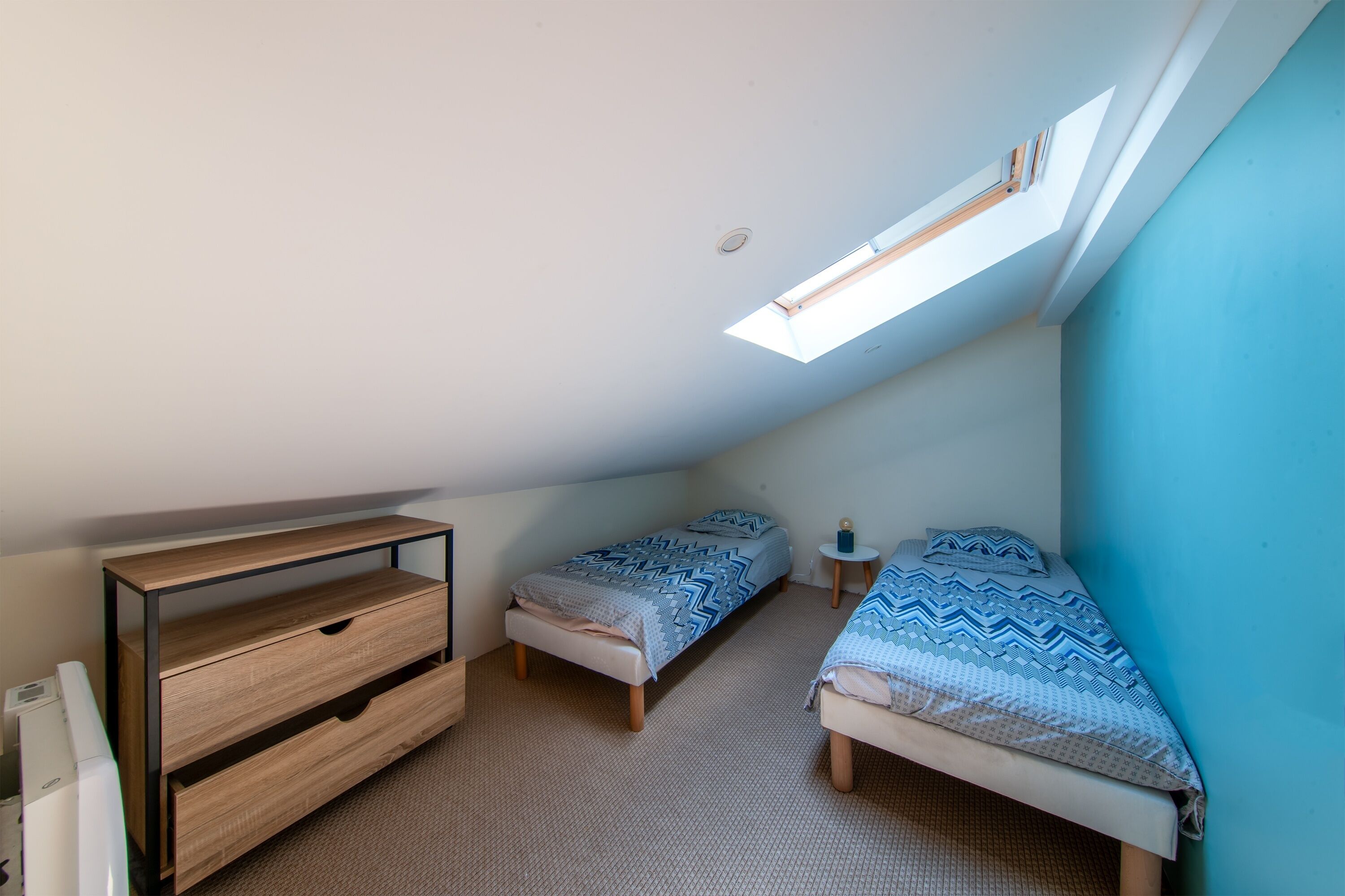 A small, well-lit room with two beds, a desk, and a skylight.
