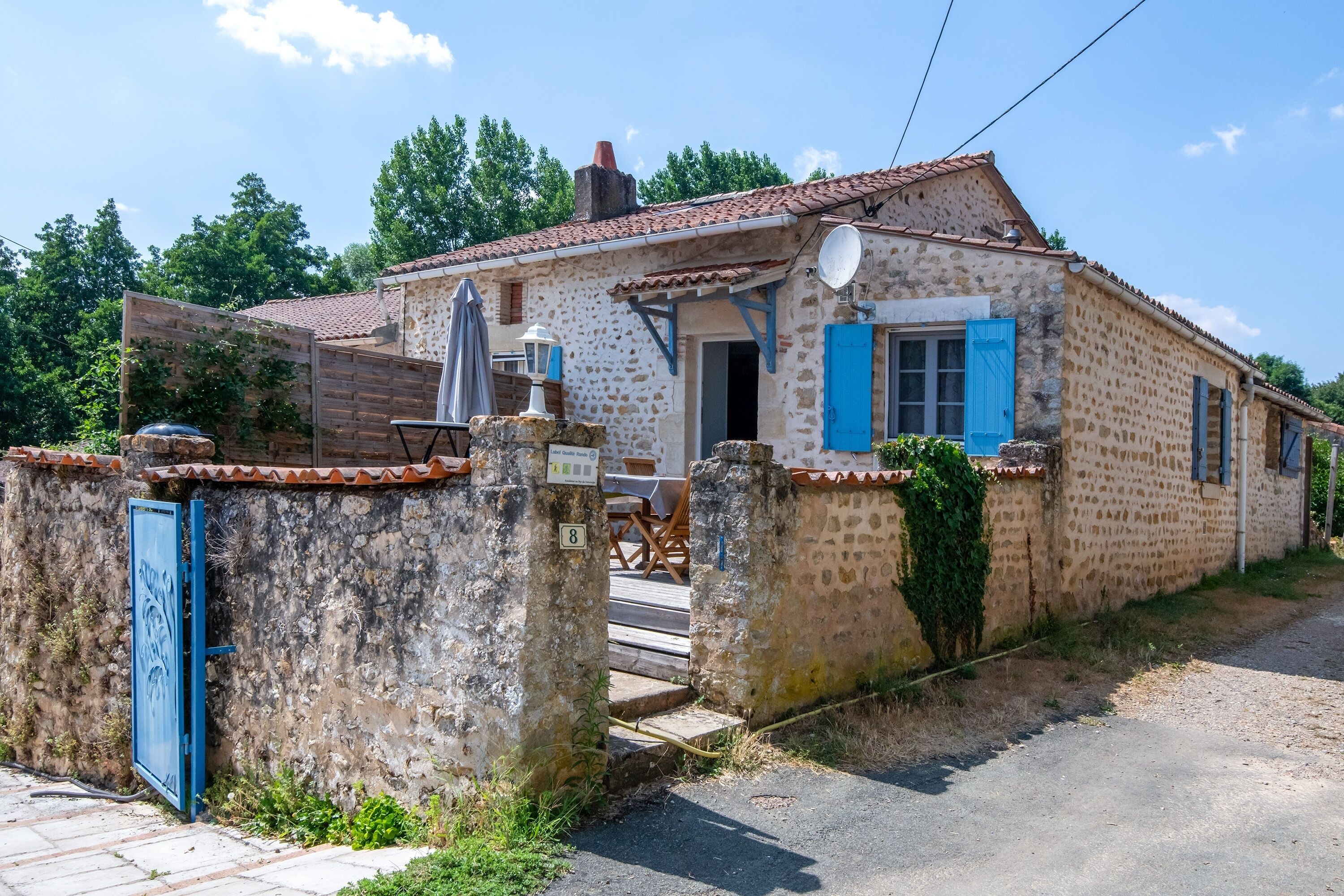 Une maison de campagne en pierre, avec un toit en tuiles, une porte bleue et une antenne parabolique.