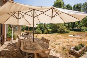 Eine Terrasse im Freien mit einem Holztisch und -stühlen, einem großen Sonnenschirm und einem gepflasterten Weg.