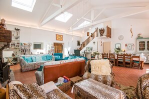 A spacious living area with a high ceiling, a staircase, and a dining area with wooden furniture. - Source Emerald - Au cœur de la nature avec vue lac (Mazamet)