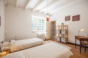 Ein Schlafzimmer mit zwei Betten, einem Heizkörper, einem Fenster, einem Regal mit Aufbewahrungsboxen und einem Schreibtisch mit Lampe.