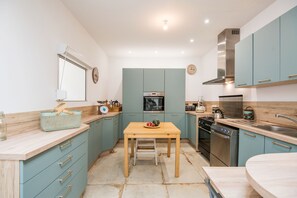 A compact kitchen with teal cabinetry, a wooden table, and modern appliances. - Source Emerald - Au cœur de la nature avec vue lac (Mazamet)