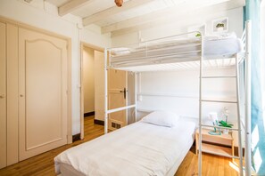 A room with a bunk bed, a single bed, a door, and a small table with a plant. - Source Emerald - Au cœur de la nature avec vue lac (Mazamet)