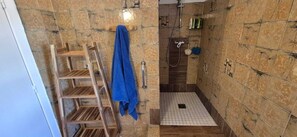 Un espace douche avec une échelle en bois et une serviette bleue, des murs carrelés et un pommeau de douche.