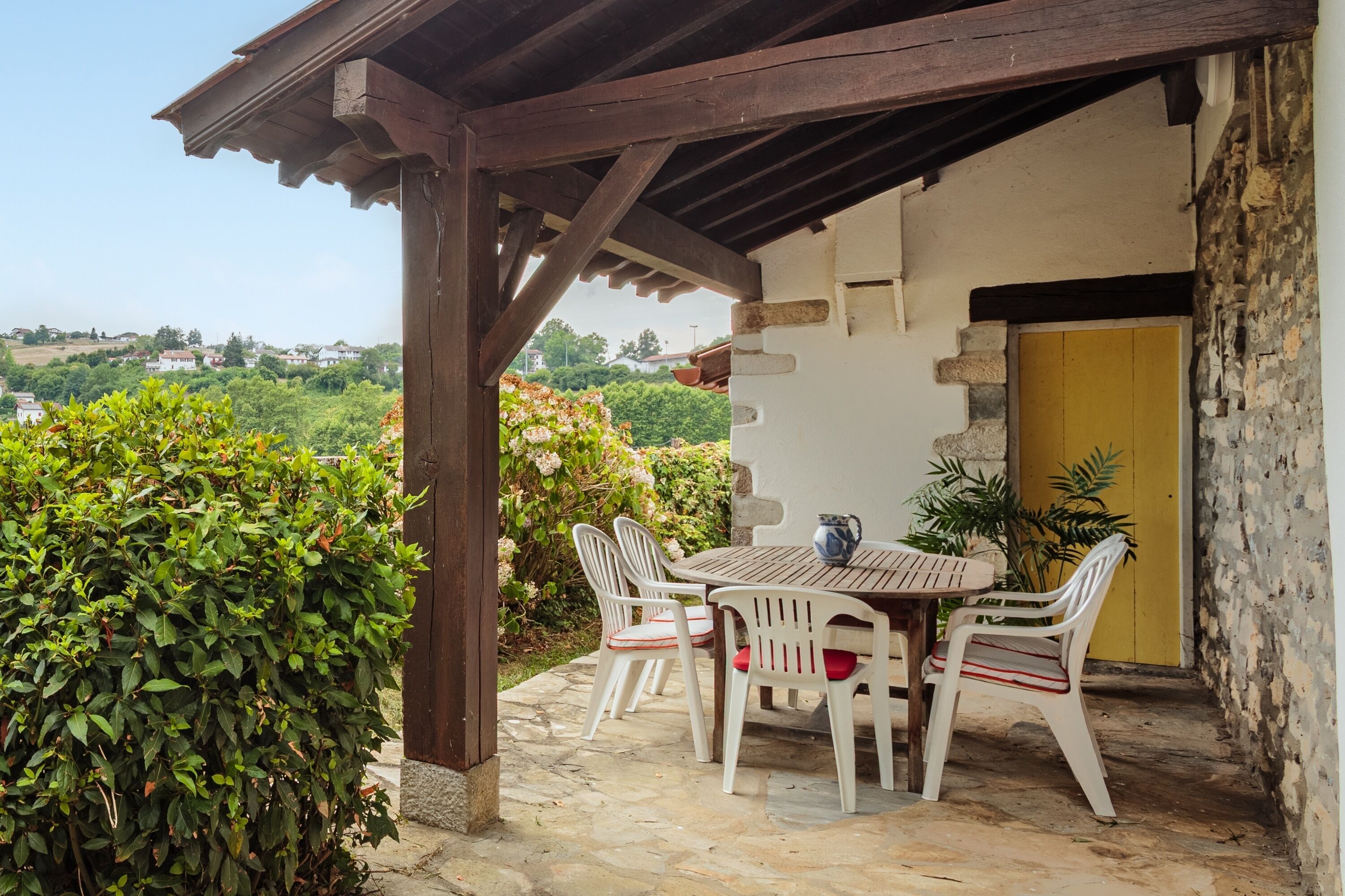 Une terrasse avec une table et des chaises, une porte jaune et une vue sur un paysage verdoyant.