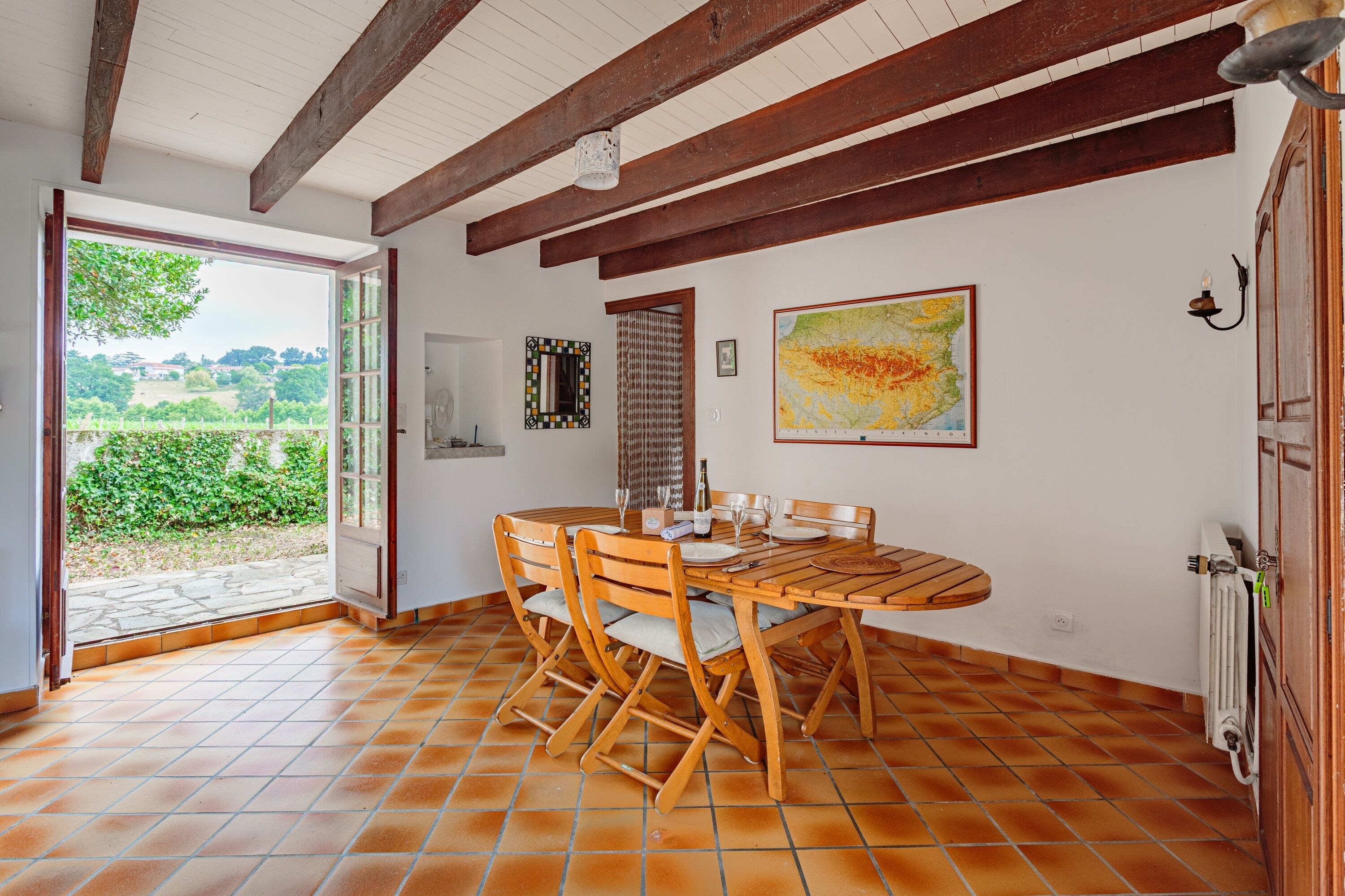 A dining area with a wooden table and chairs, a view through an open door, and a map on the wall.