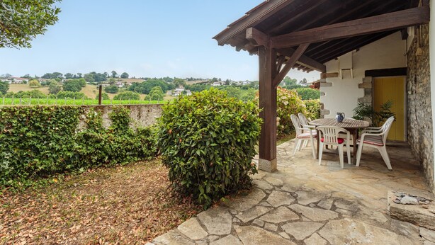 A covered outdoor seating area with stone flooring, a table, and chairs.