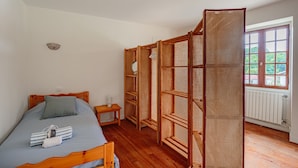 A bedroom with a wooden bed, a small bedside table, a wardrobe with a mirror, and a window with a view of greenery.